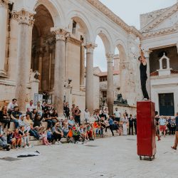 Un homme debout sur un casier en métal sur une place de style italien.