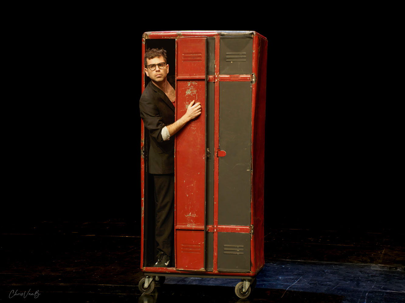 Un homme, sur scène, sort d'un casier en métal.