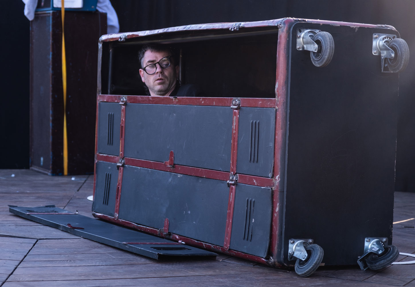 Un homme dans un casier en métal, vertical, laisse apercevoir la tête, lunettes penchées.