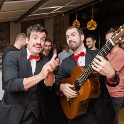 2 musiciens en costard jouent. L'un à la guitare et l'autre chante en tapant dans les mains.