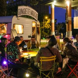 Plusieurs personnes attablées dans une guinguette assistent à un tour de magie.