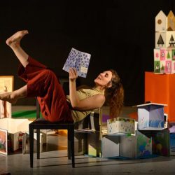 Une femme allongée sur une chaise lit un livre à voix haute.