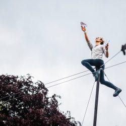 Une voltigeuse en équilibre sur le haut d'un poteau lance un avion en papier.