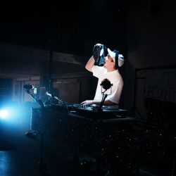 Derrière les platines le DJ semble manger du matériel.