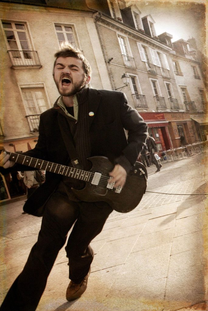 Un homme en costume cri dans la rue une guitare à la main.