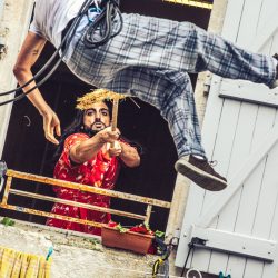 Un homme à la fenêtre d'une maison repousse avec un balai, un homme qui voltige à l'extérieur.