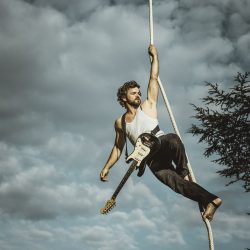 Un circassien suspendu sur une corde porte une guitare.