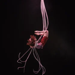 Une femme fait de la voltige sur scène. Elle est cambrée en hauteur, les lumières sont roses.