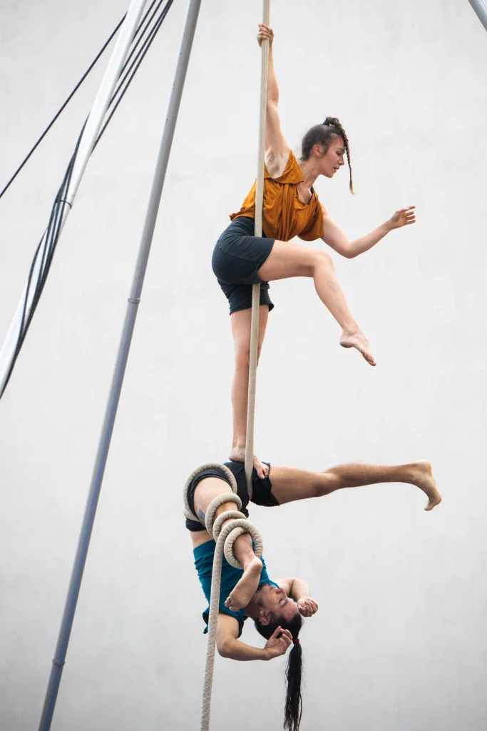 Deux artistes en équilibre l'un sur l'autre, font de la danse sur cordes. L'une est debout. Le deuxième en dessous sur le dos et une jambe enroulée dans une corde.