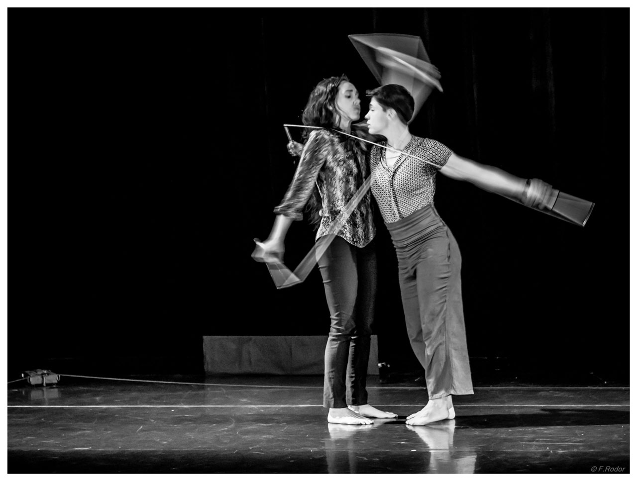 Photo du spectacle. En salle, sur scène.
Image en noir et blanc des 2 circassiens avec un léger flou. 
Ils continuent les acrobaties avec 2 cordes de diabolos qui pour l'une les sépare, pour l'autre les réunie.  