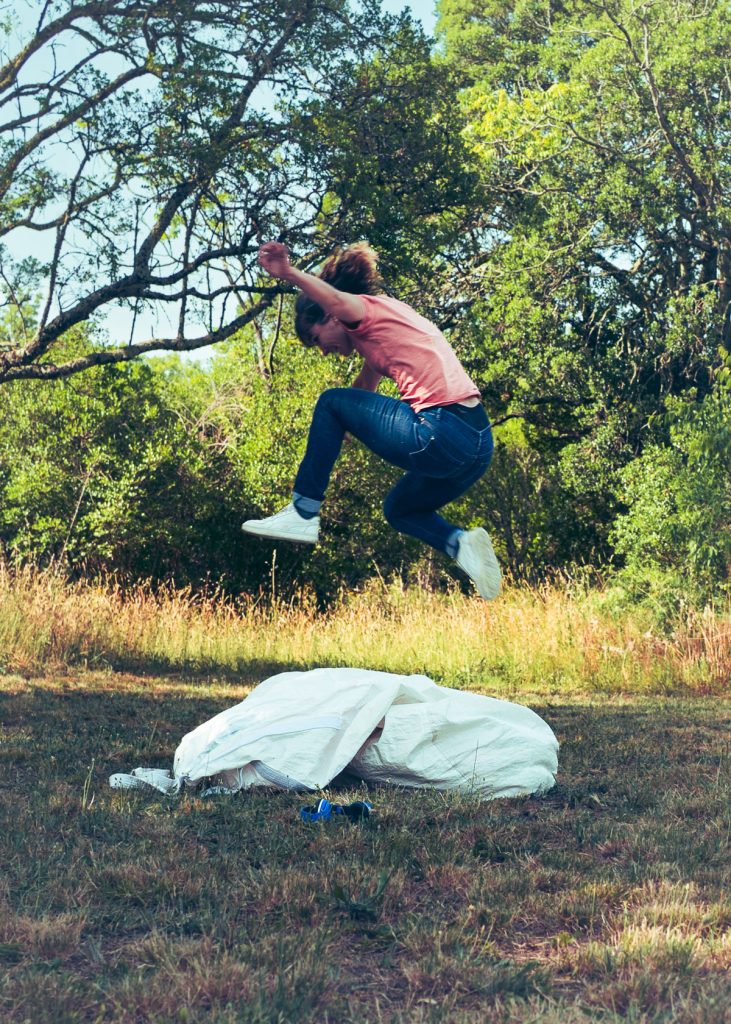 Dans la campagne, une femme saute au-dessus d'un grand sac.