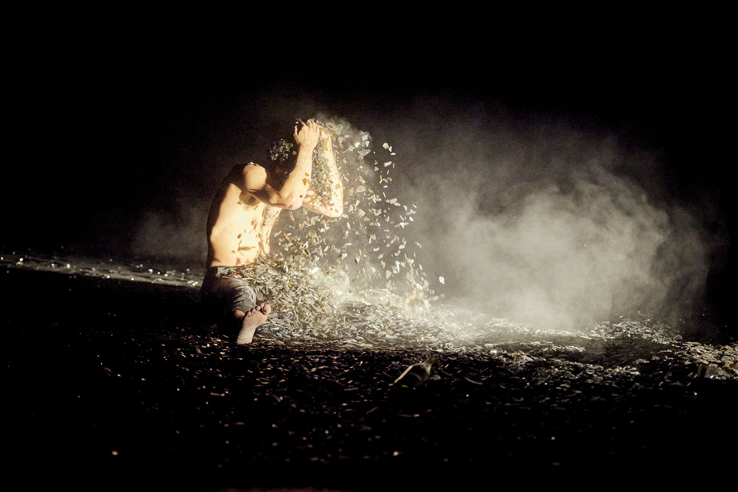 Le circassien assis sur scène prend un tas de verre dans ses mains et se le verse dessus.