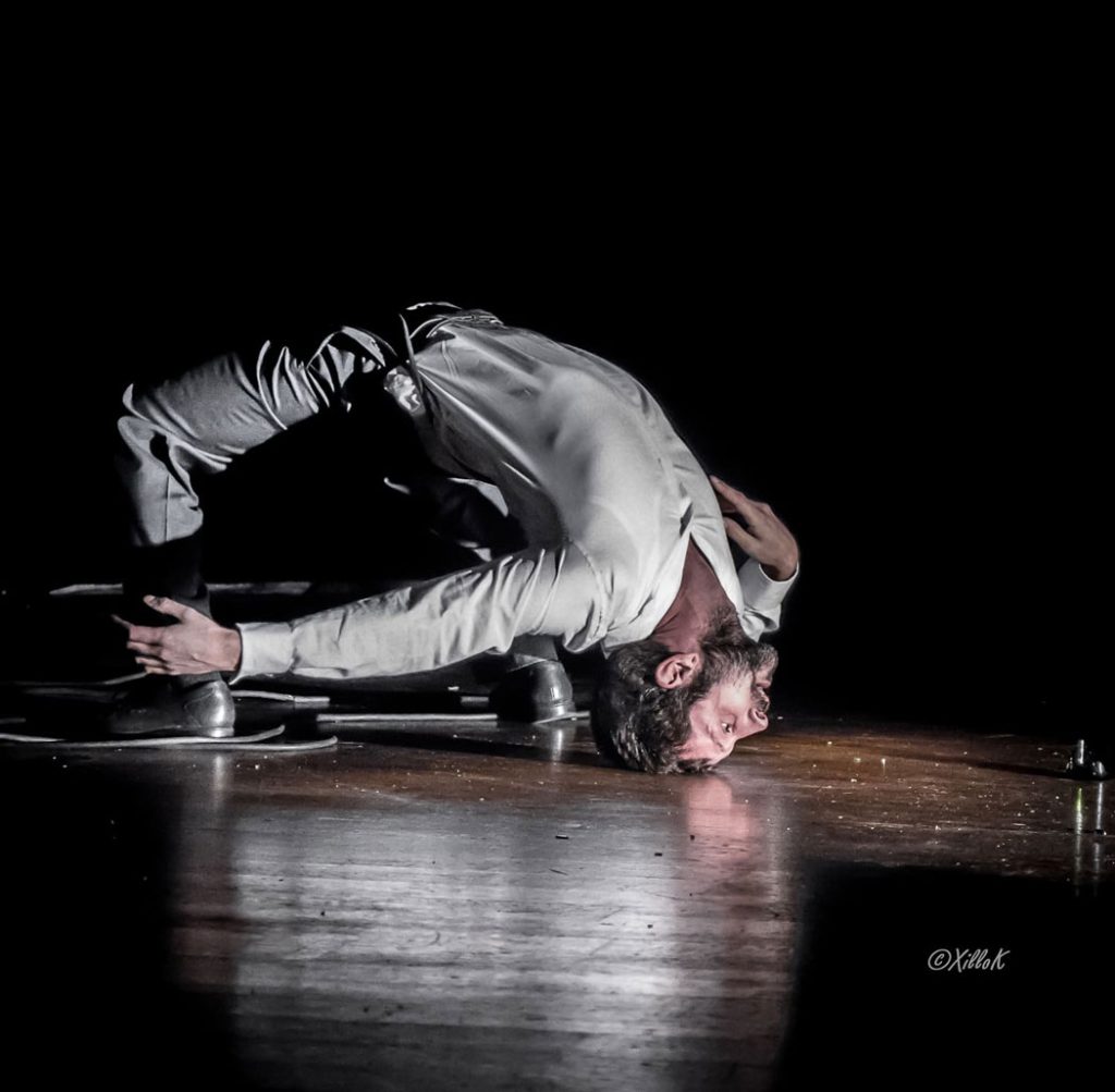 Un circassien éclairé en blanc fait le pont avec tout son corps.