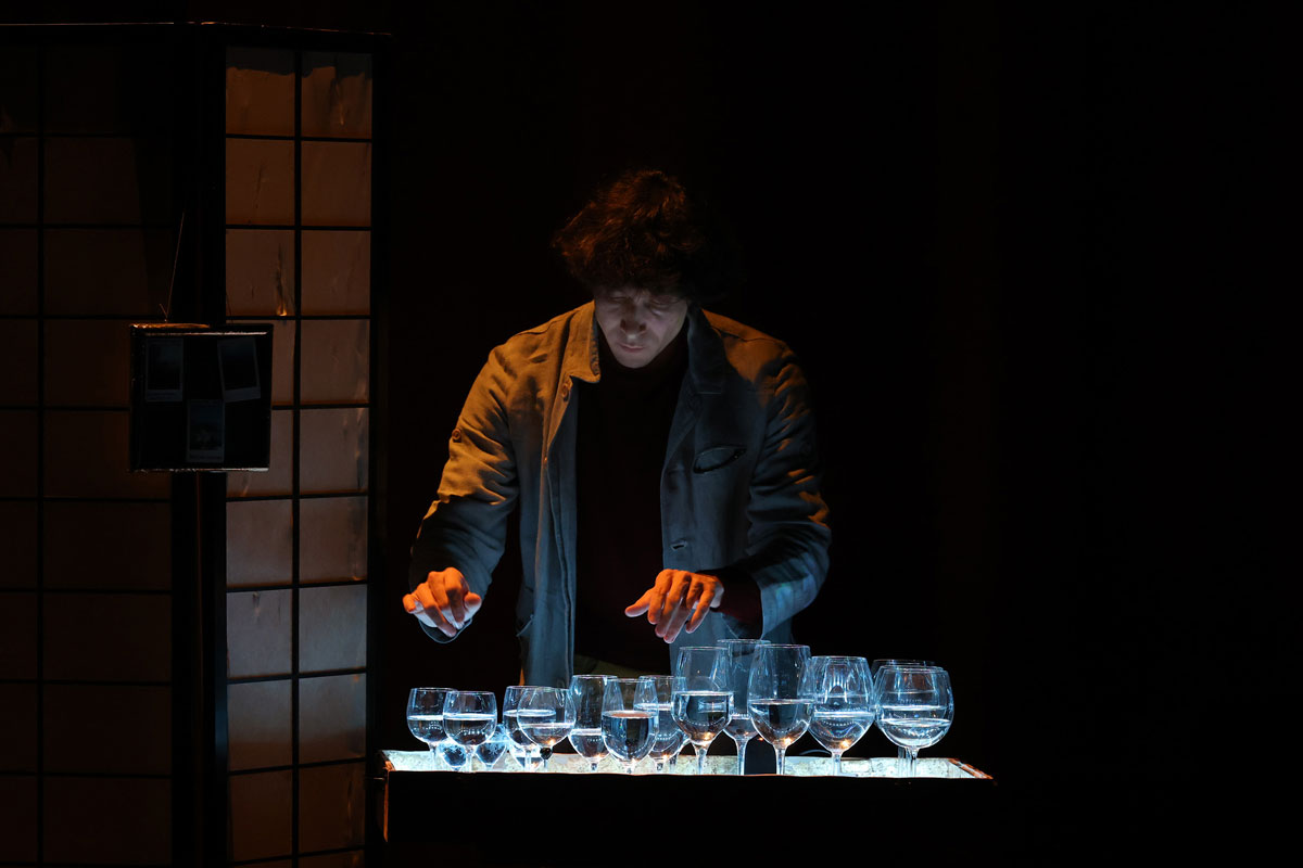 Le circassien se tient devant des verres à pied remplit d'eau éclairés en bleu.