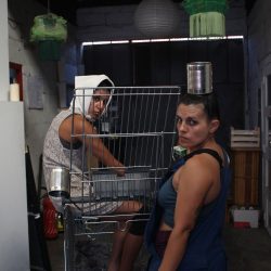 Dans une réserve, 2 femmes, le regard perçant, se tiennent près d’un caddie. Une a un foulard sur la tête.