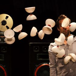 Devant un magnétophone à bande, un circassien a une dizaine de diabolos qui lui passent devant le visage.