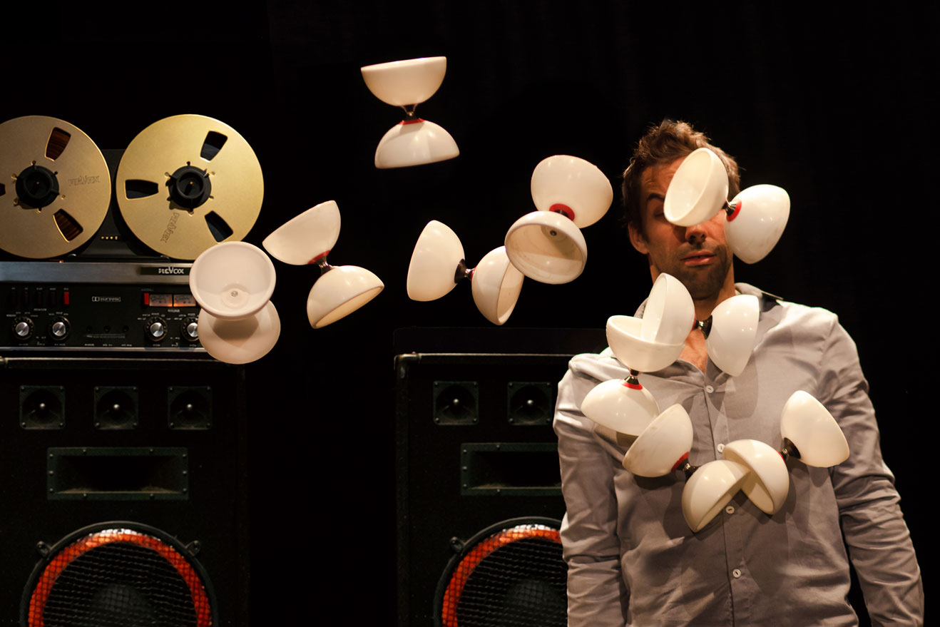 Devant un magnétophone à bande, un circassien a une dizaine de diabolos qui lui passent devant le visage. 