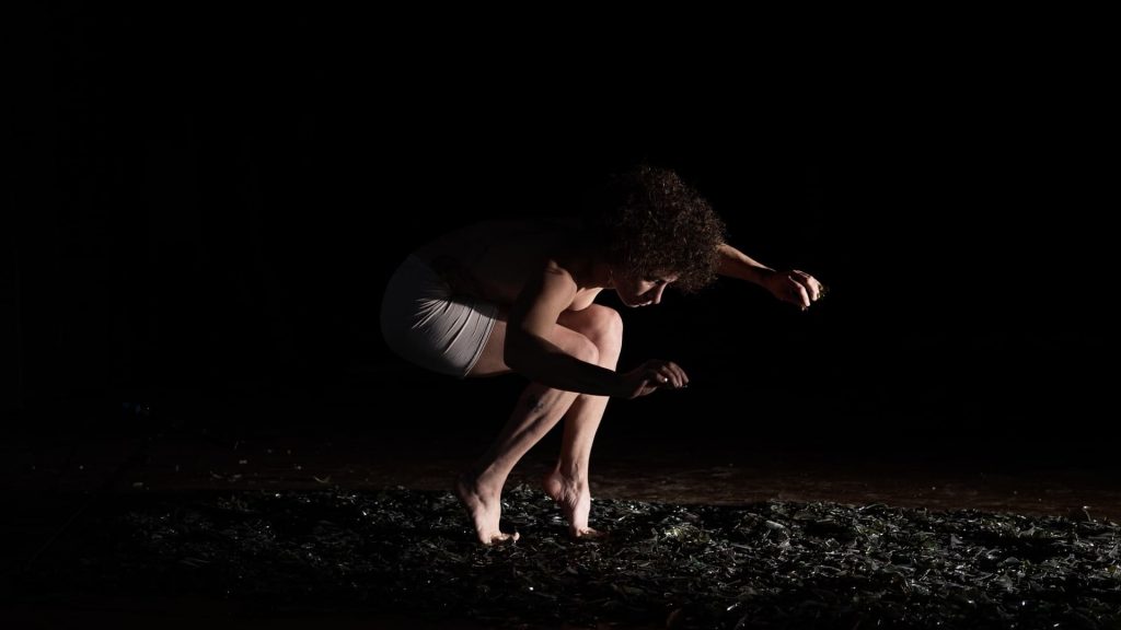 Une circassienne accroupie marche avec la pointe des pieds sur un tapie de verre.
