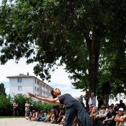 Une danseuse debout, tenue noire, cambrée et bassin en avant est entourée du public.