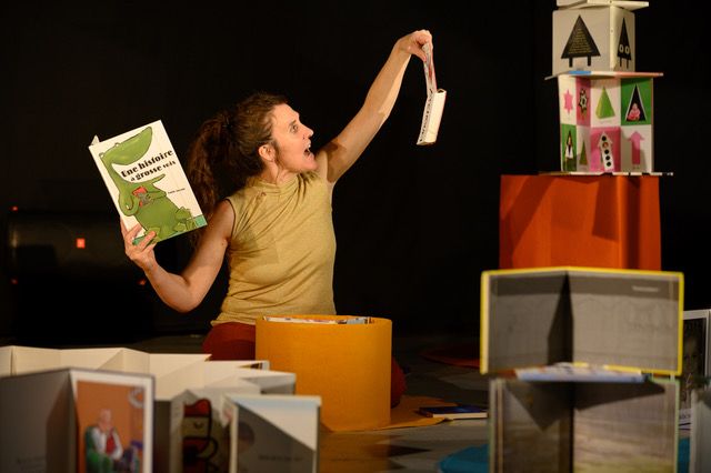 Une femme tient 2 livre de manière non conventionnelle. Elle est entourée d'une pyramide et d'un tourniquet de livre.