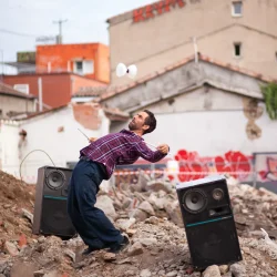 Un homme jongle avec son diabolo sur un tas de gravas, ses 2 grosses enceintes derrière lui.