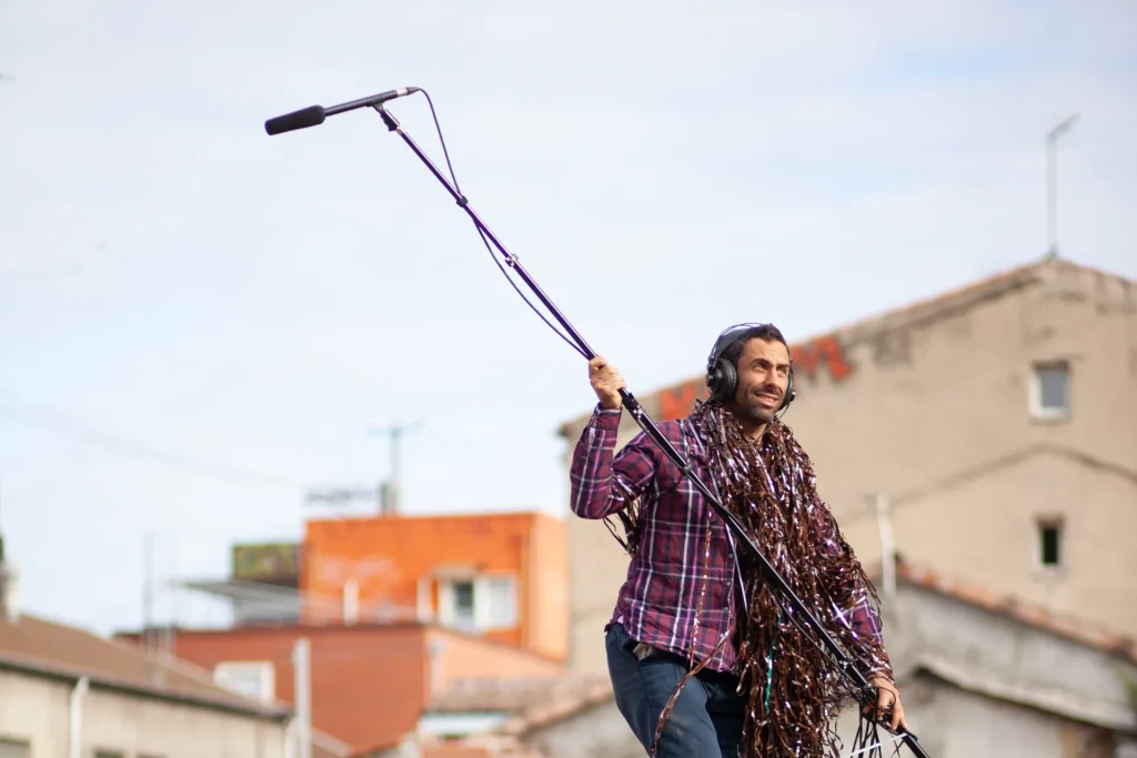 Un homme avance, casque sur la tête et micro perche dans les bras en extérieur pour écouter les sons qui l'entourent.