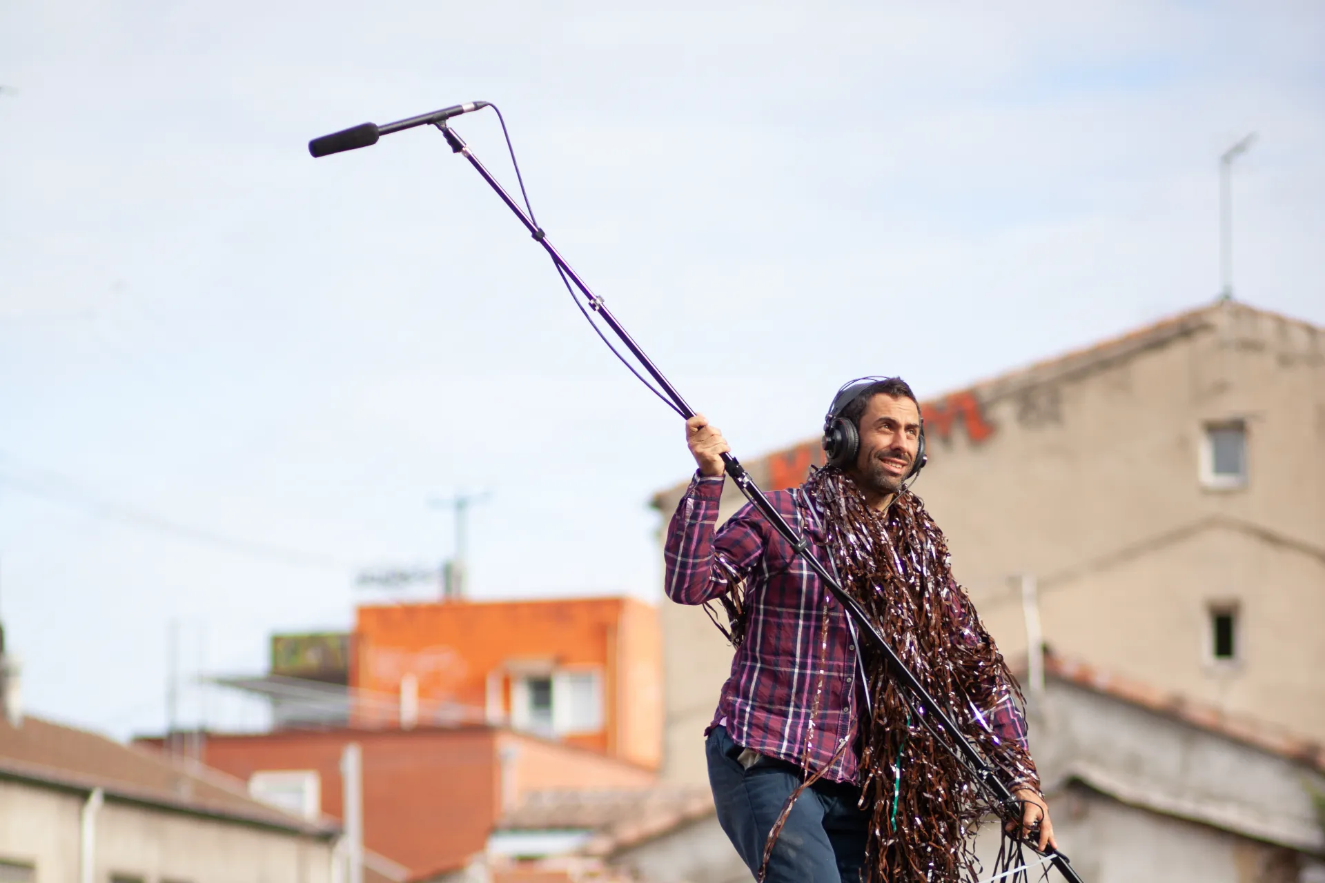 Un homme avance, casque sur la tête et micro perche dans les bras en extérieur pour écouter les sons qui l'entourent.