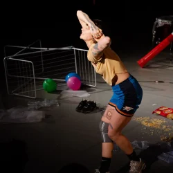 Une circassienne se contorsionne sur une scène où sont présents divers objets de la vie de tous les jours.